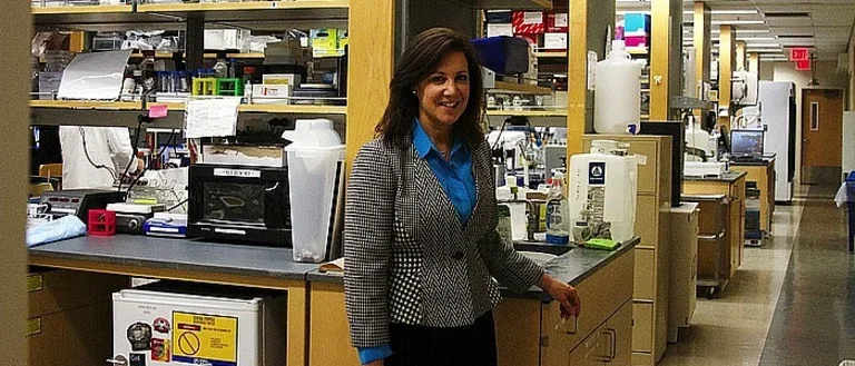 A researcher stands in front of aisles of researching equipment and stations.