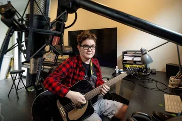 Cooper Jones in a red flannel shirt playing guitar in a studio.