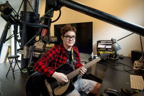 Cooper Jones in a red flannel shirt playing guitar in a studio.