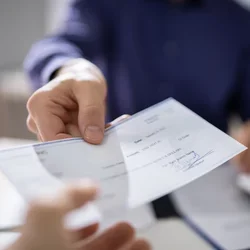 A business person's outstretched arm is seen handing a check to another person's outstretched arm.
